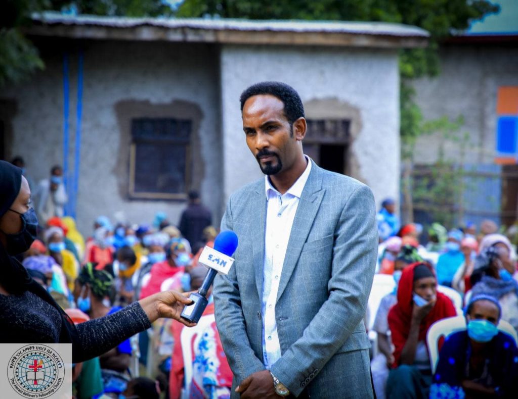 A bilnd man from the church in Awassa speaking to a journalist. There is a colorful crowd behind him.