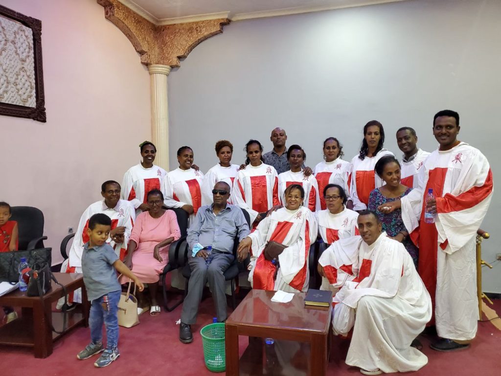 Berhanu sitting with about 15 members of the choir, dressed in white and red robes.